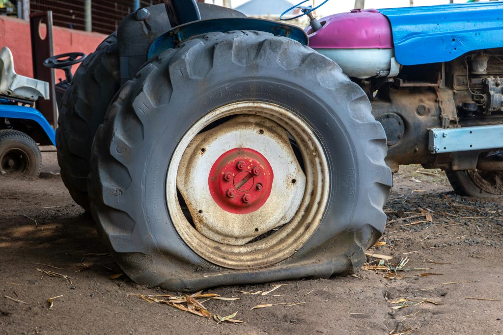 Close-up of an old tractor with a flat tire in a rustic barn, showing wear and time effects.